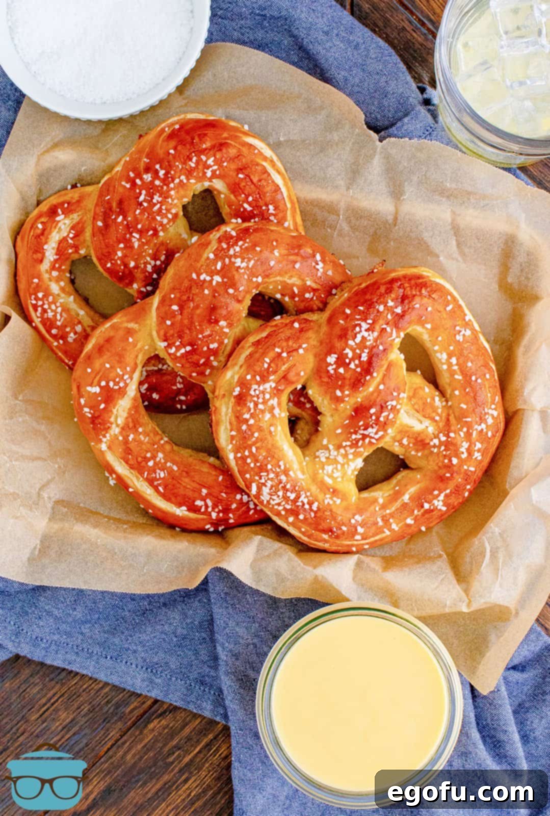 Overhead view of three golden Homemade Soft Pretzels, ready to be enjoyed with cheese sauce, arranged on a parchment-lined tray.