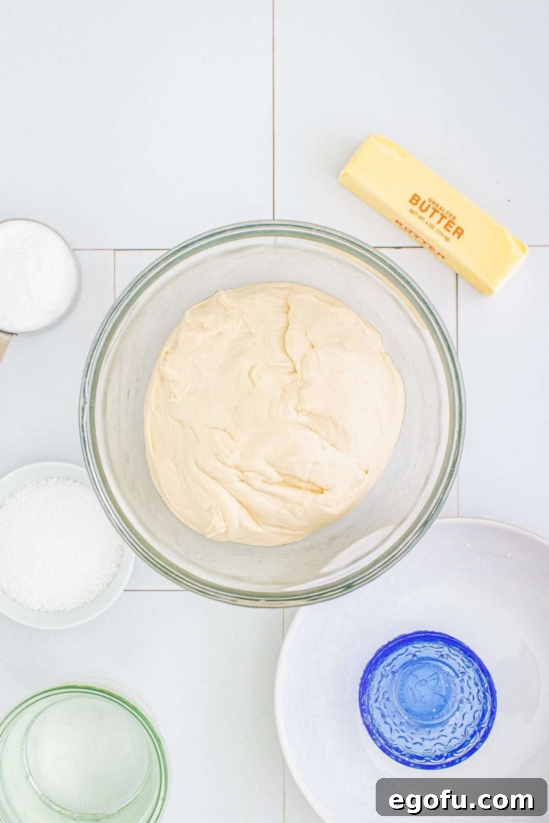 Dough ball resting in a greased bowl, covered with plastic wrap.
