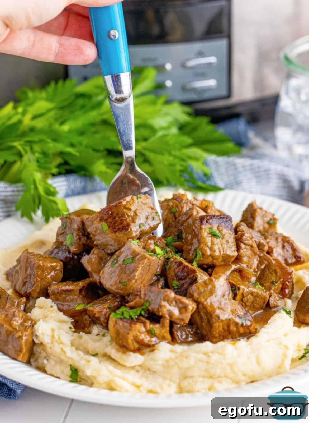 Slow Cooker Garlic Butter Steak Bites over mashed potatoes with fork going into steak, showcasing the tenderness and rich gravy.