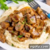 Slow Cooker Garlic Butter Steak Bites close up square image on plate with mashed potatoes and fork.