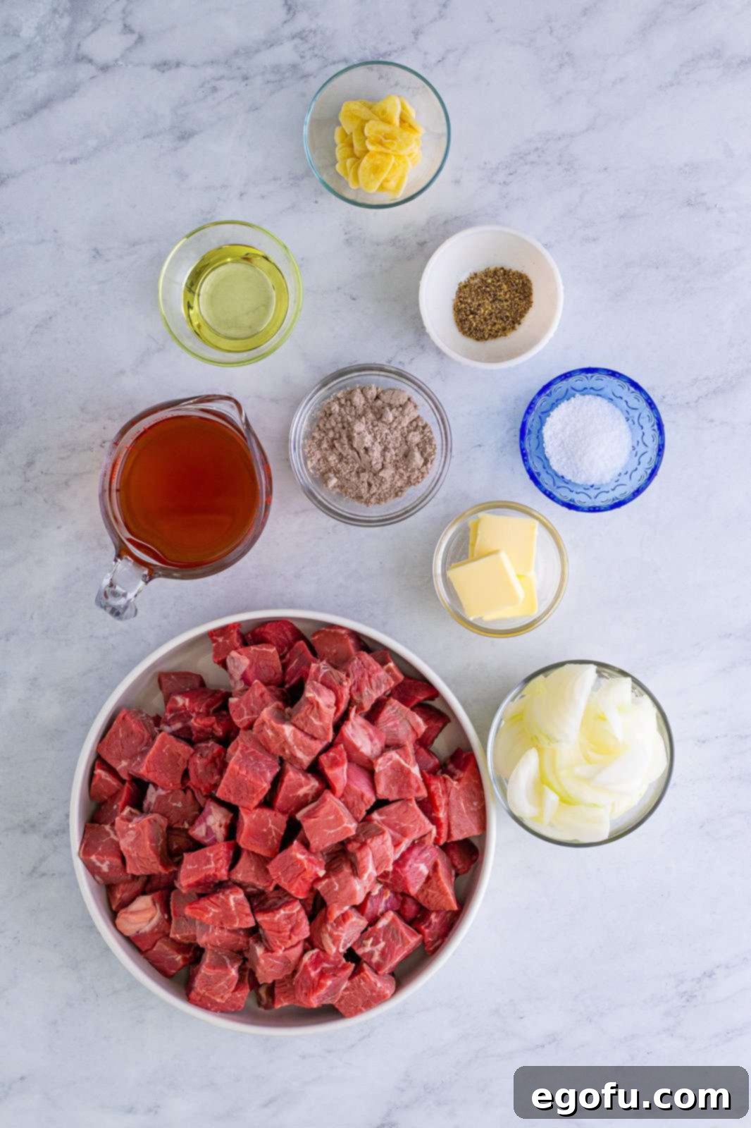 Ingredients laid out for Slow Cooker Garlic Butter Steak Bites: sirloin steak, kosher salt, pepper, vegetable oil, sweet onion, garlic, unsalted beef stock, au jus gravy mix, unsalted butter and fresh parsley.