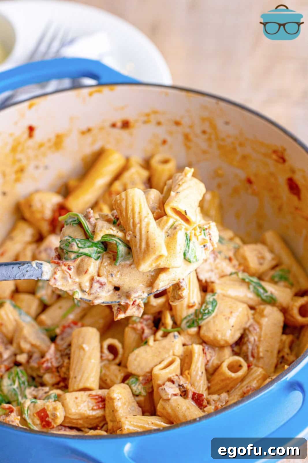 Serving spoon holding up some of the Tuscan Chicken Pasta out of the dutch oven, showing the rich, creamy texture.