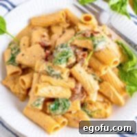 Square image close up of Tuscan Chicken Pasta on white plate with fork.