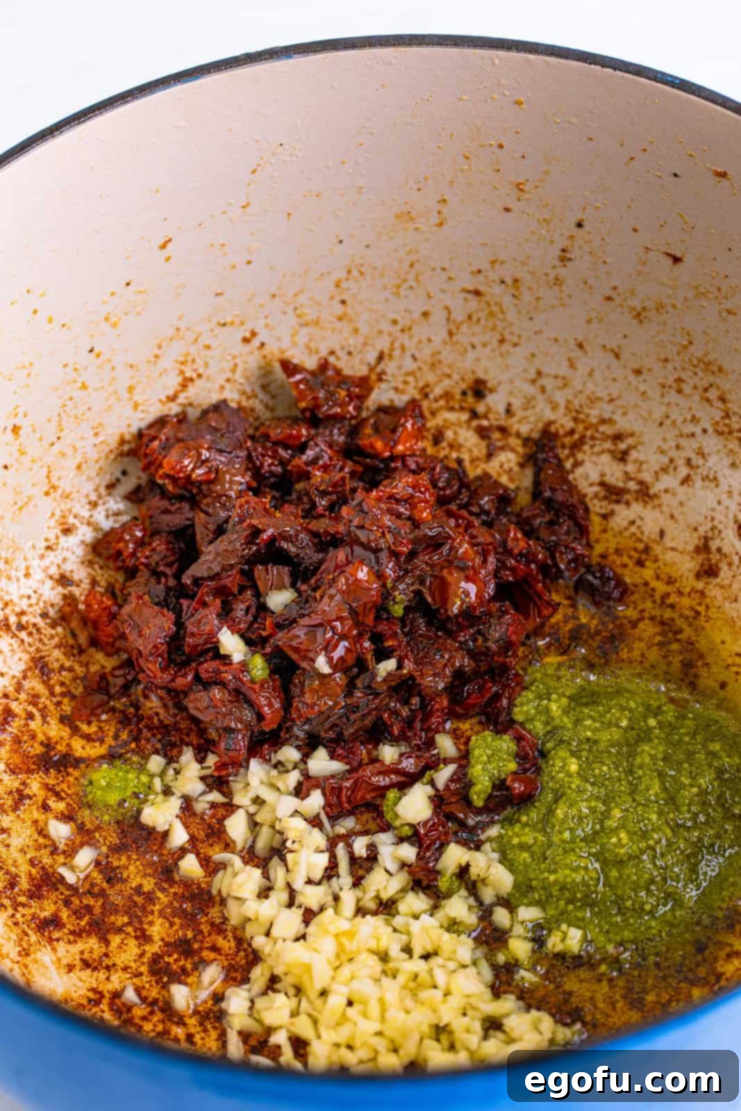 Sun-dried tomatoes, garlic, and pesto added to dutch oven, being stirred.