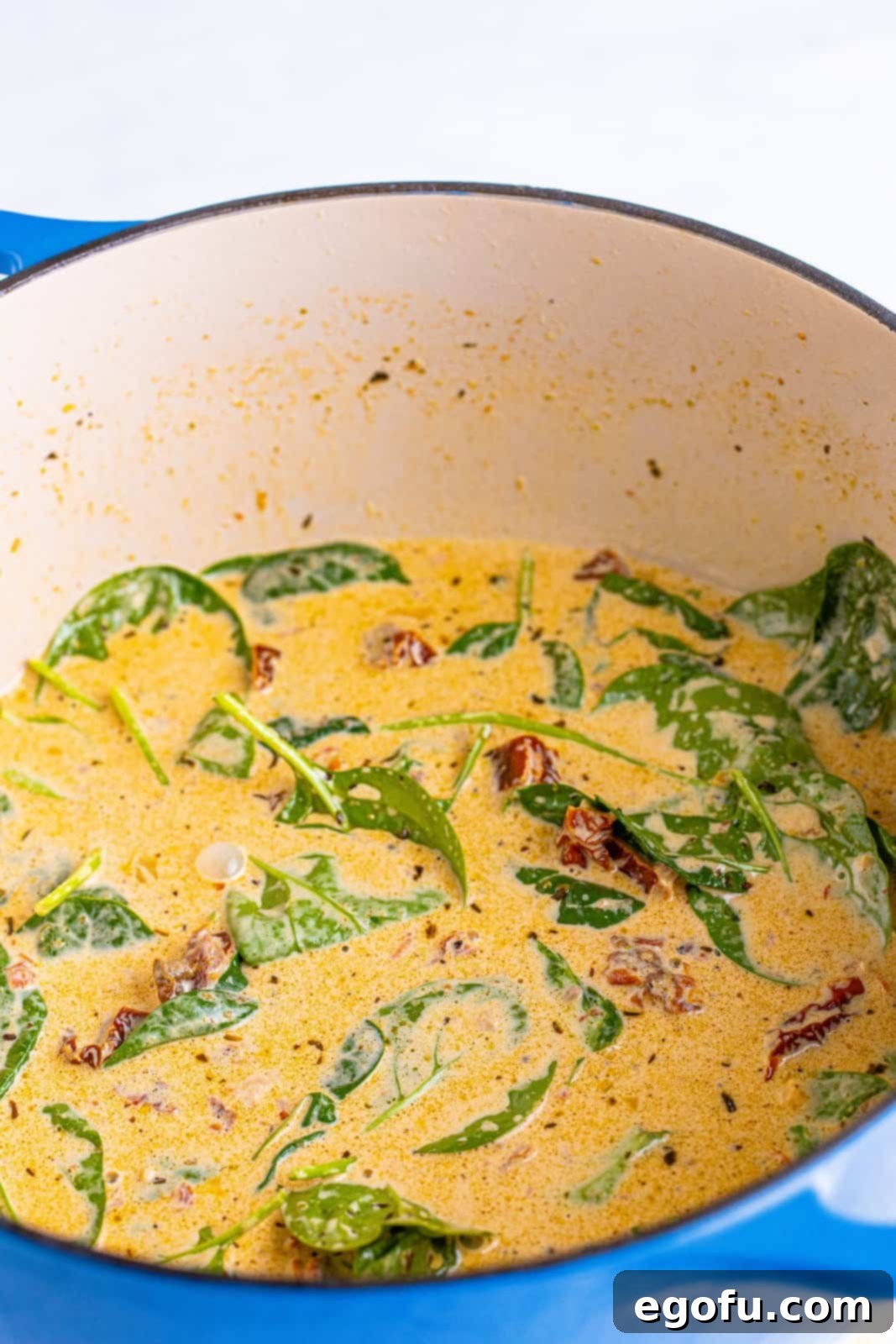 Baby spinach, salt, and pepper added to dutch oven mixture and stirred in, showing the spinach beginning to wilt.
