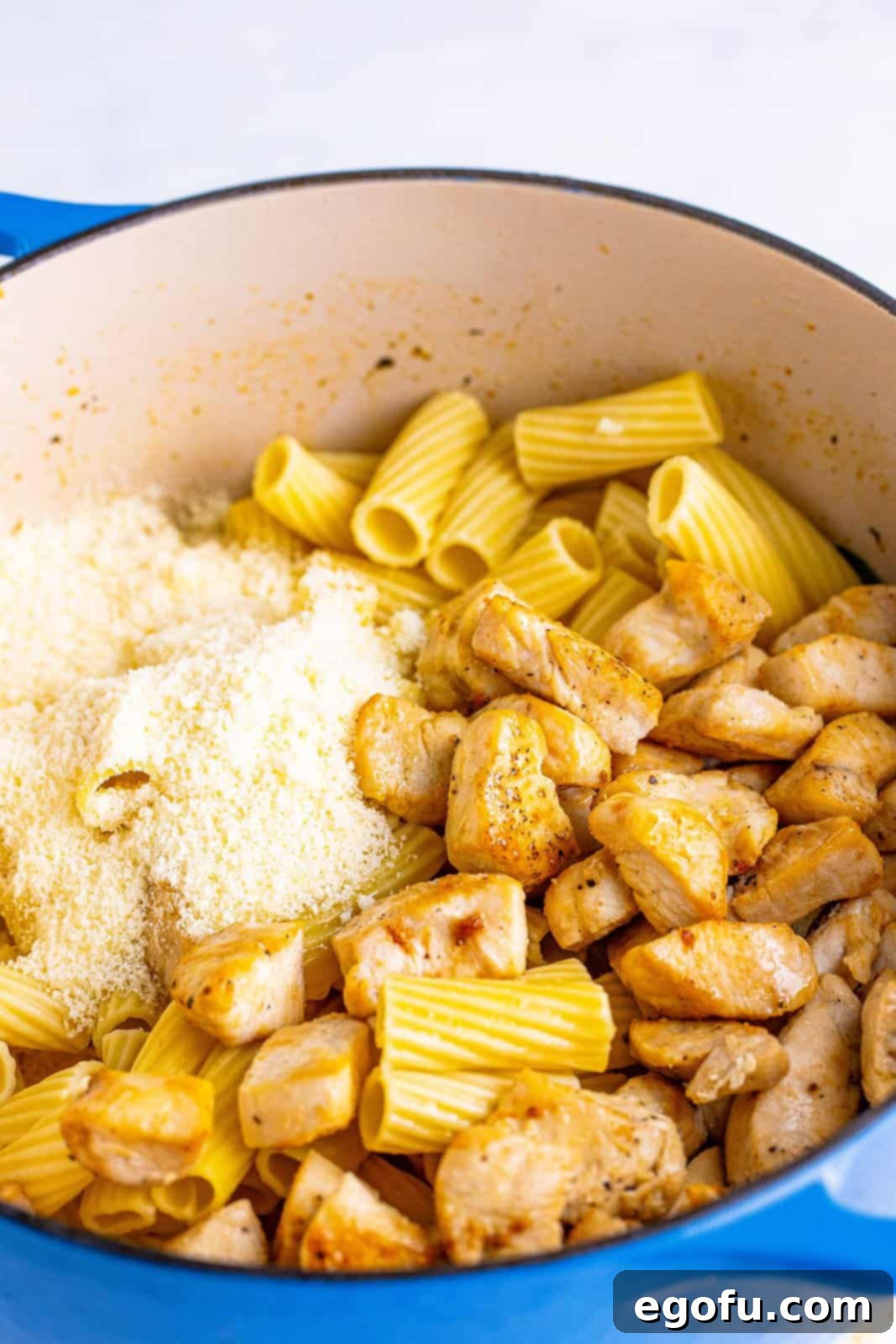 Cooked chicken, parmesan cheese, and cooked rigatoni added to dutch oven, being stirred to combine.