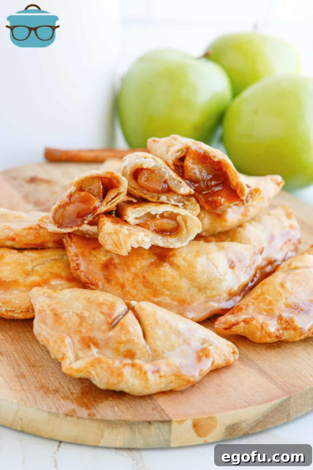 Air Fryer Apple Hand Pies stacked on wooden board with some hand pies split open showing inside.