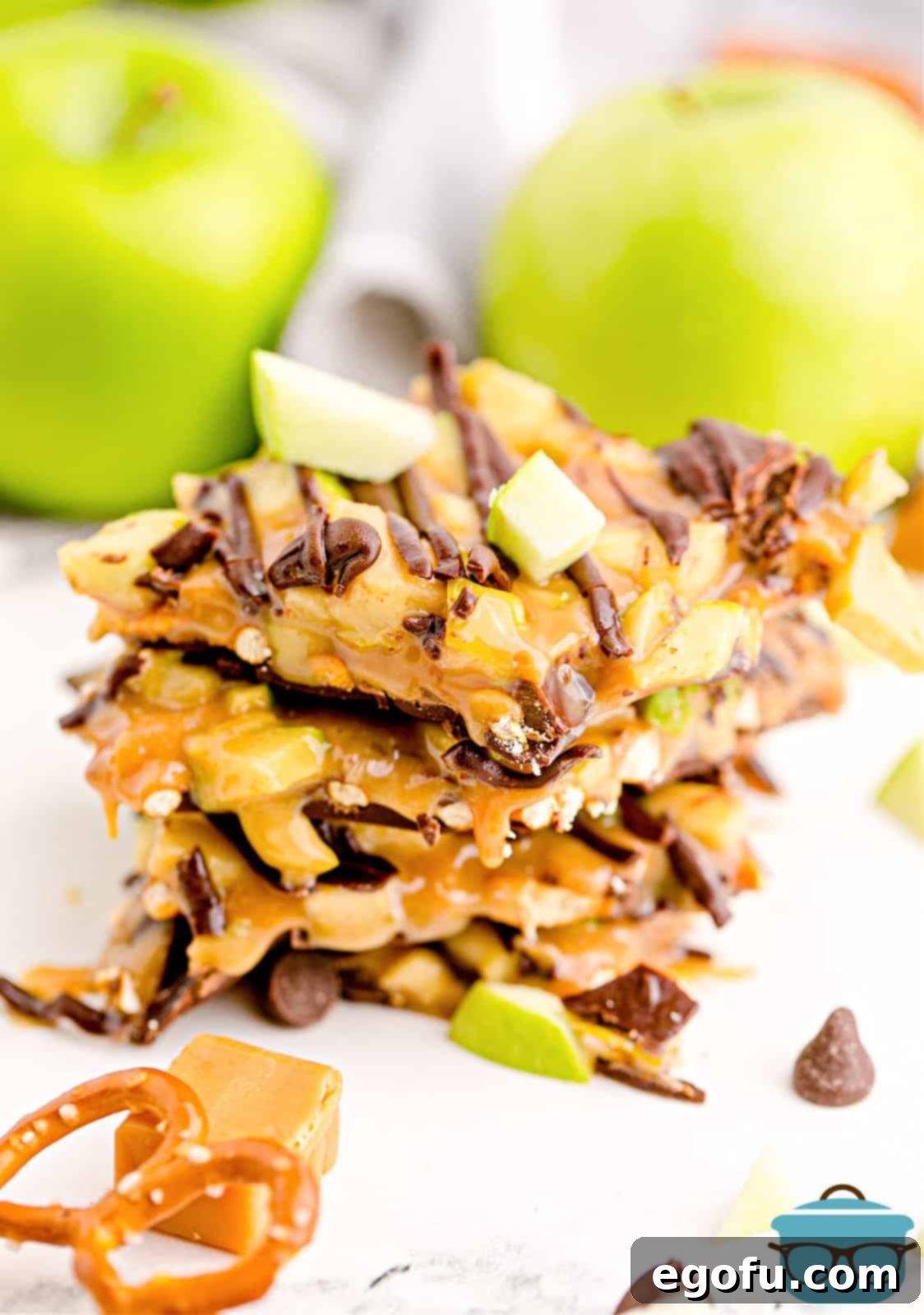 Stacked slices of delicious homemade Caramel Apple Bark, showcasing its layers of chocolate, pretzels, caramel, and apples.