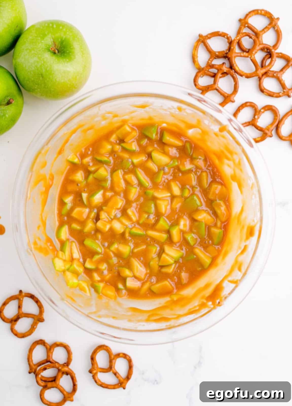 Diced apples mixed thoroughly into melted caramel in a bowl.