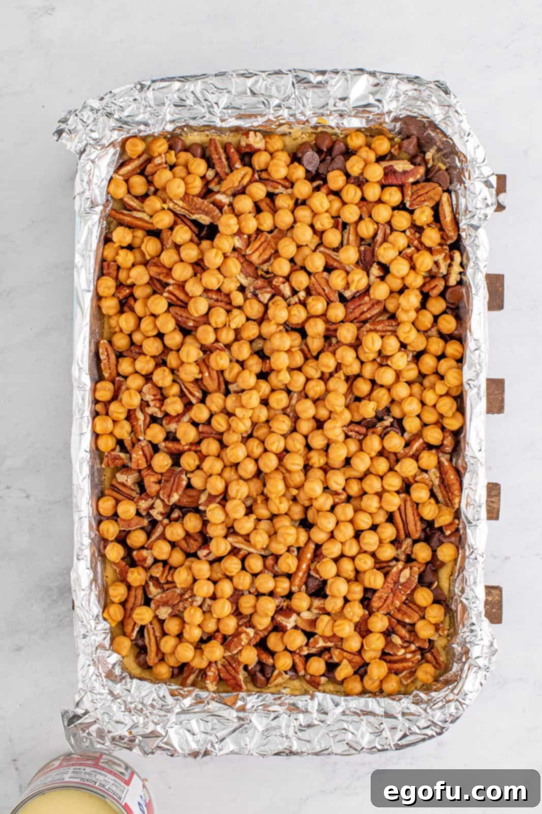Layers of chocolate chips, chopped pecans, and caramel bits sprinkled generously over the baked crust in the baking dish.