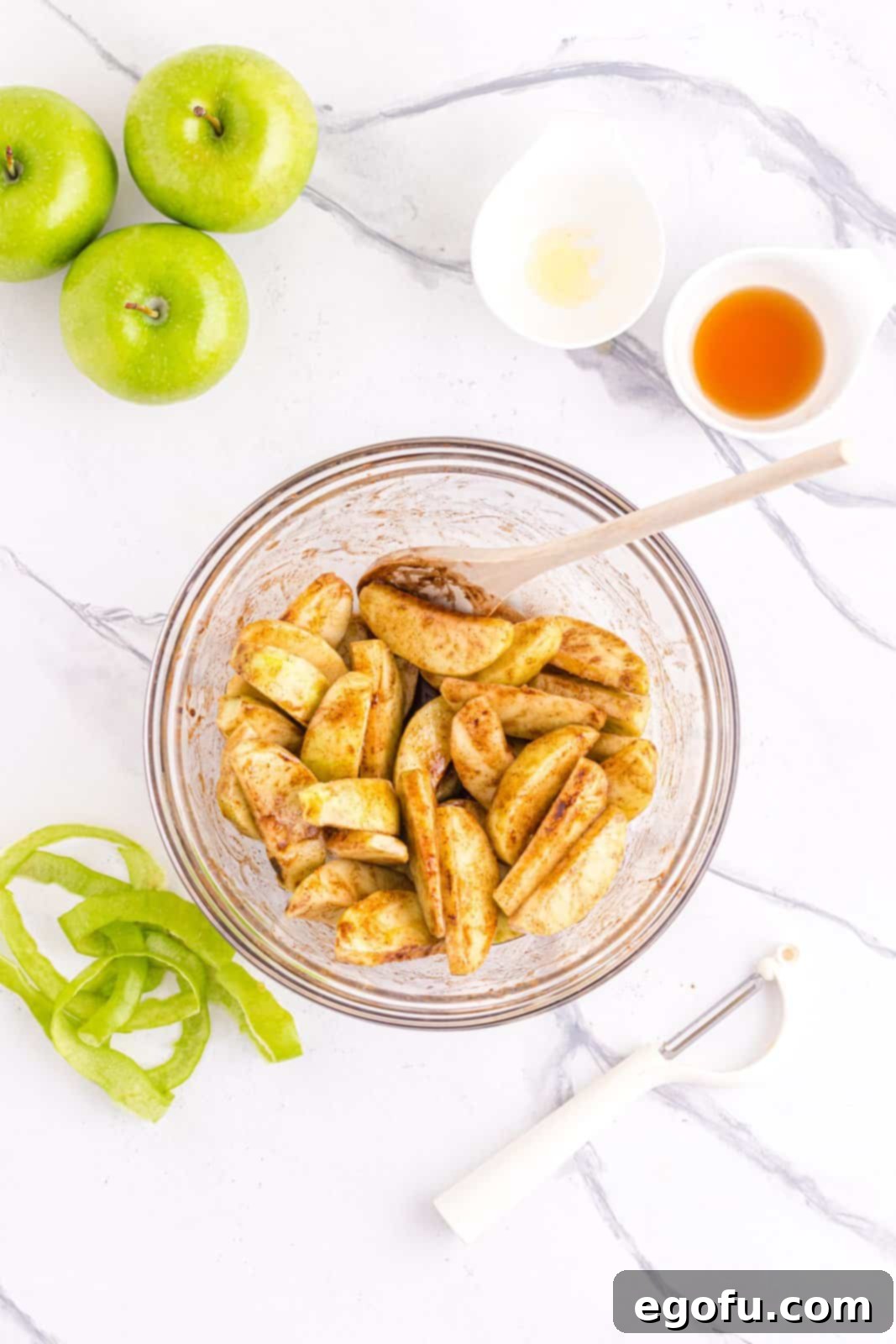 Apples in bowl mixed together with brown sugar, cinnamon, salt, maple syrup and butter, perfectly coated and ready for cooking.