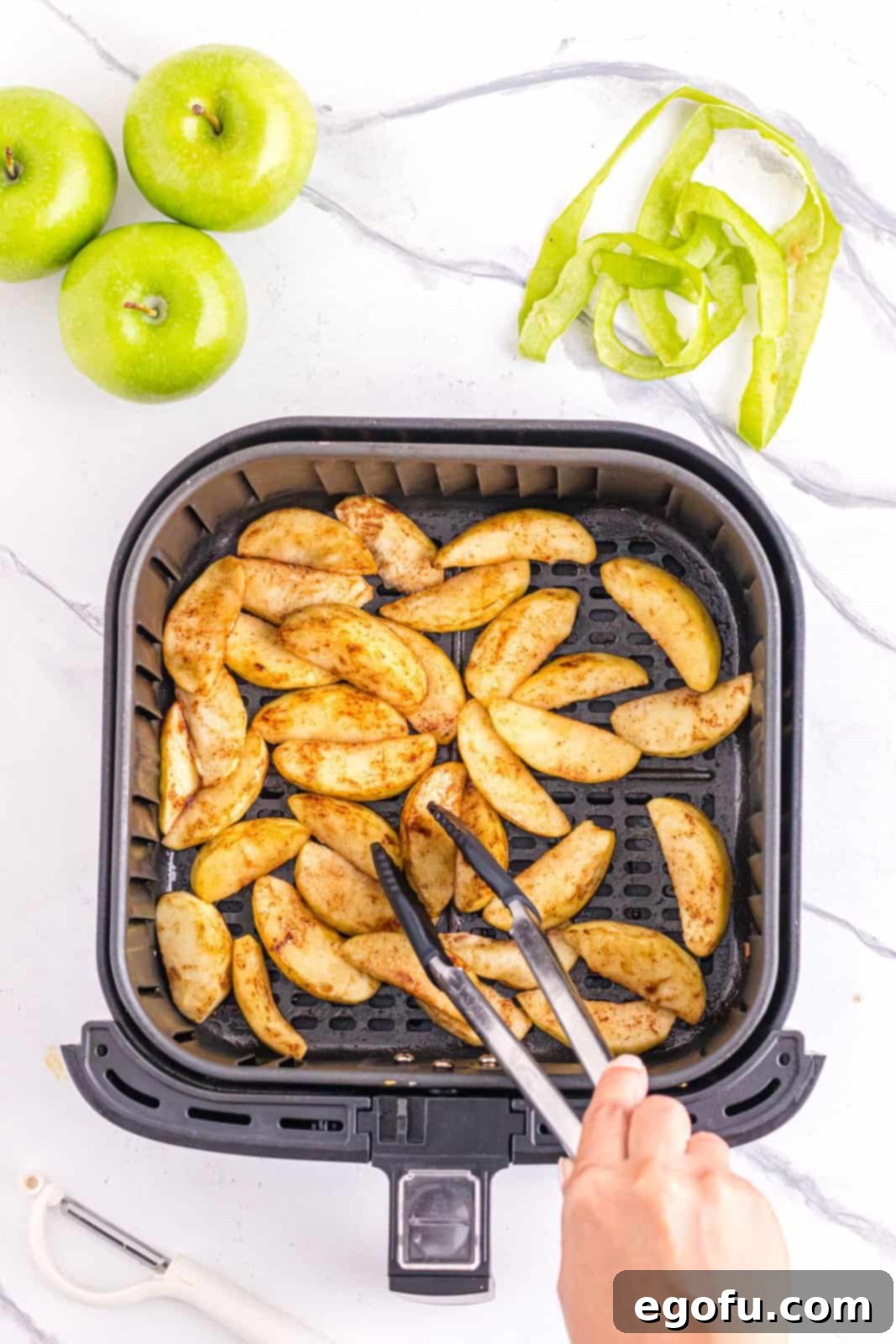 Apples being flipped in air fryer, demonstrating the mid-cooking stage for even browning.
