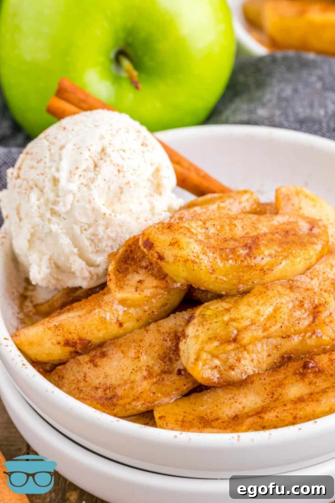 Air Fryer Fried Apples in white stacked bowls with scoop of ice cream and cinnamon stick, a delightful presentation.