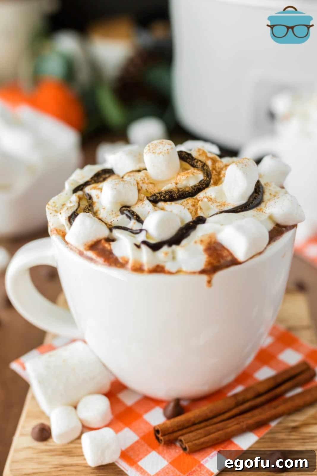 A steaming mug of Crock Pot Pumpkin Hot Chocolate, garnished with whipped cream and a sprinkle of cinnamon, sitting on a wooden surface.
