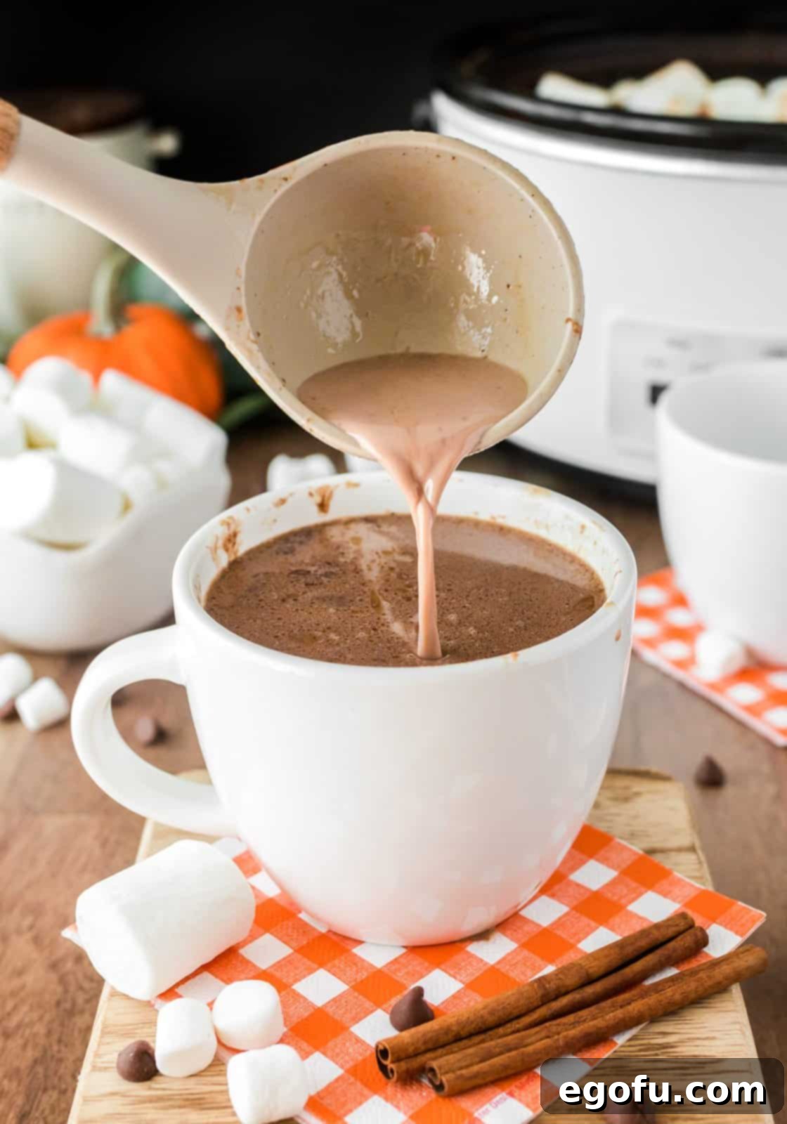 A ladle is pouring the freshly made, steaming Crock Pot Pumpkin Hot Chocolate from the slow cooker into a festive mug, ready for serving.