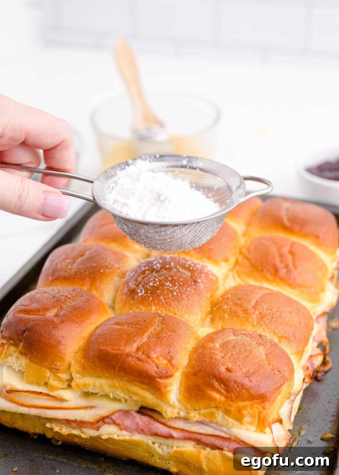 Powdered sugar being sprinkled over baked sandwiches.