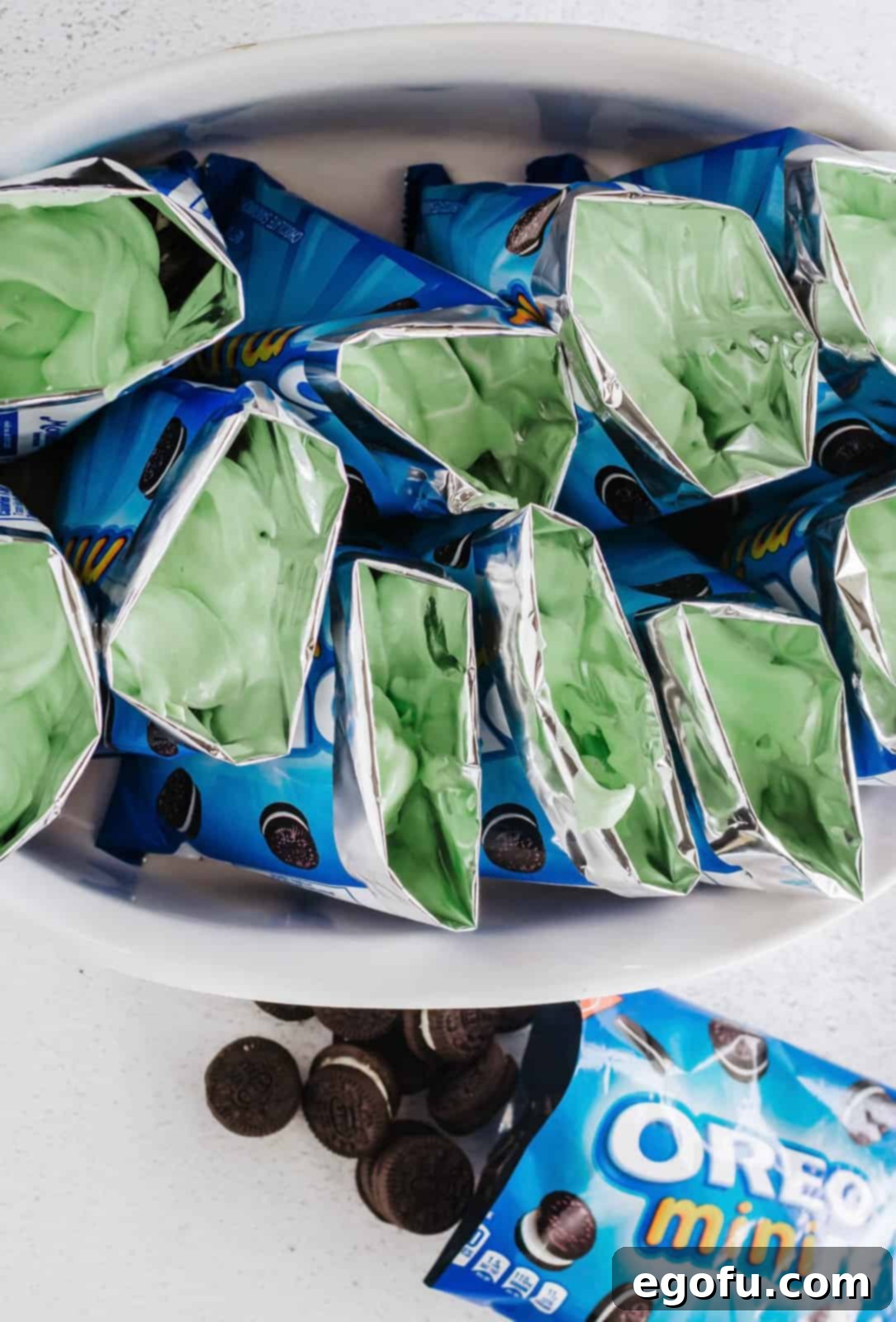Prepared green pudding being spooned into individual mini Oreo cookie snack bags.