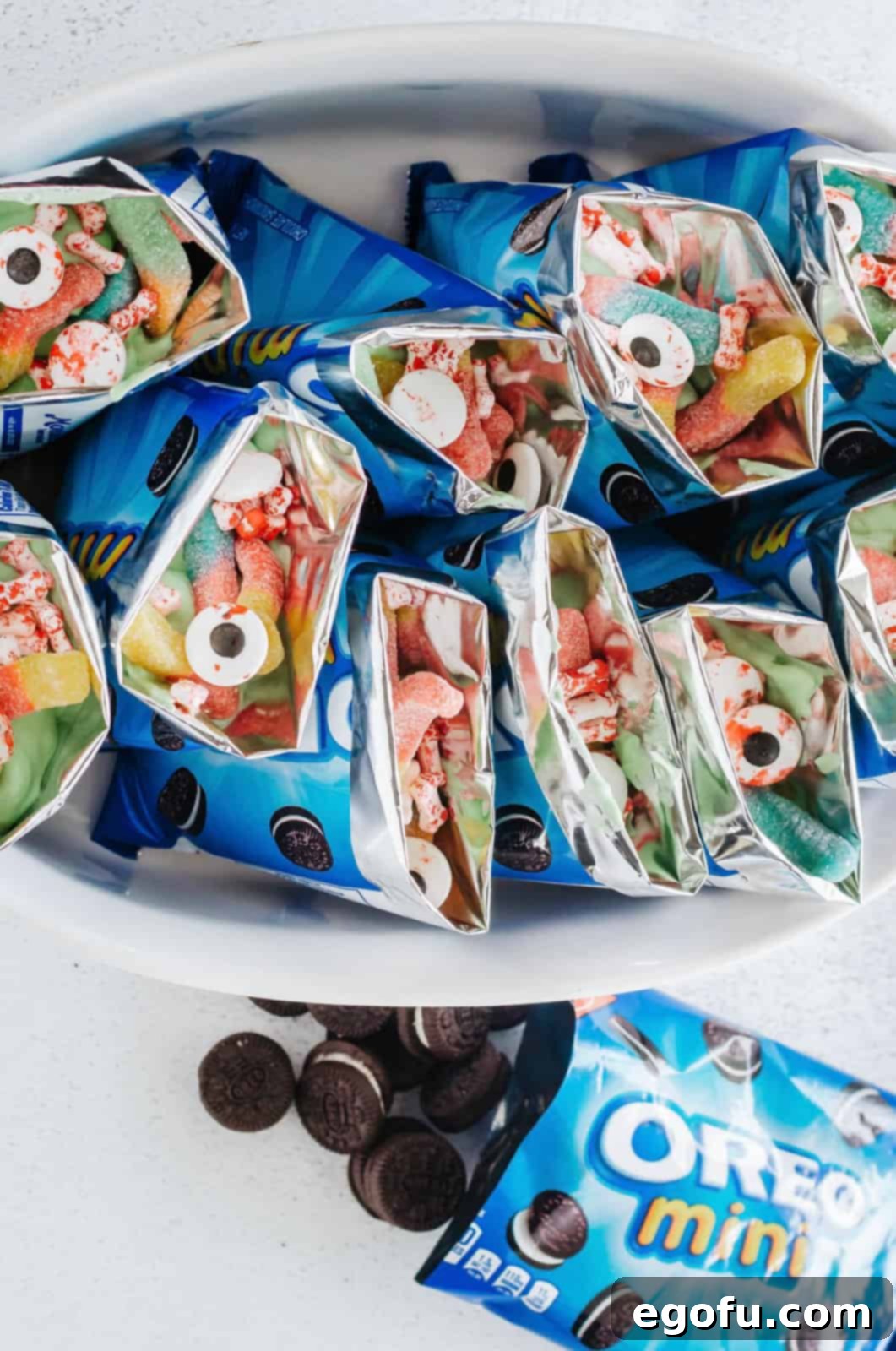 Halloween candies including gummy worms, candy eyes, and candy bones being added as toppings to the pudding-filled Oreo bags.