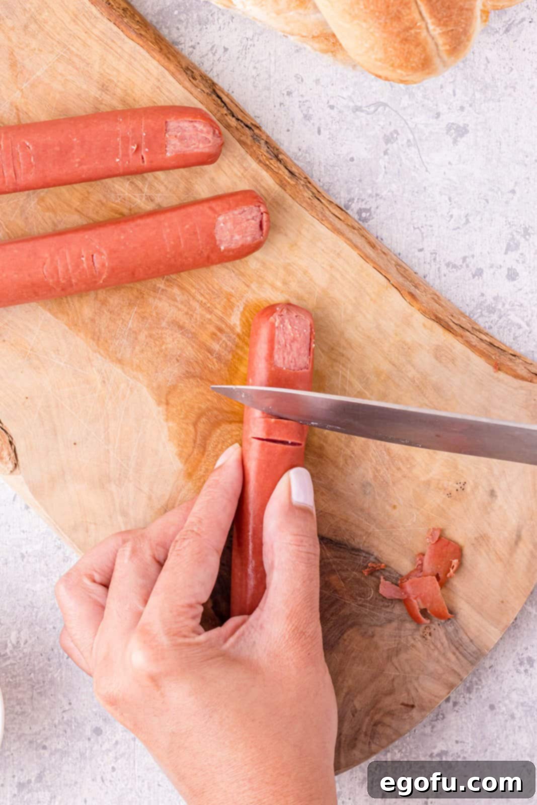 Knife cutting the upper knuckle creases in hot dog.