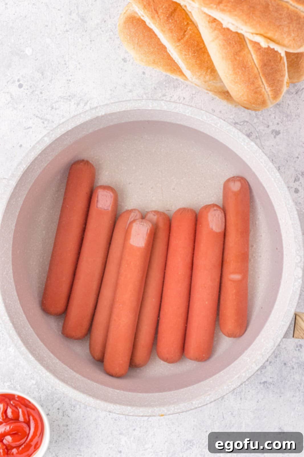 Hot dogs being boiled in pan.
