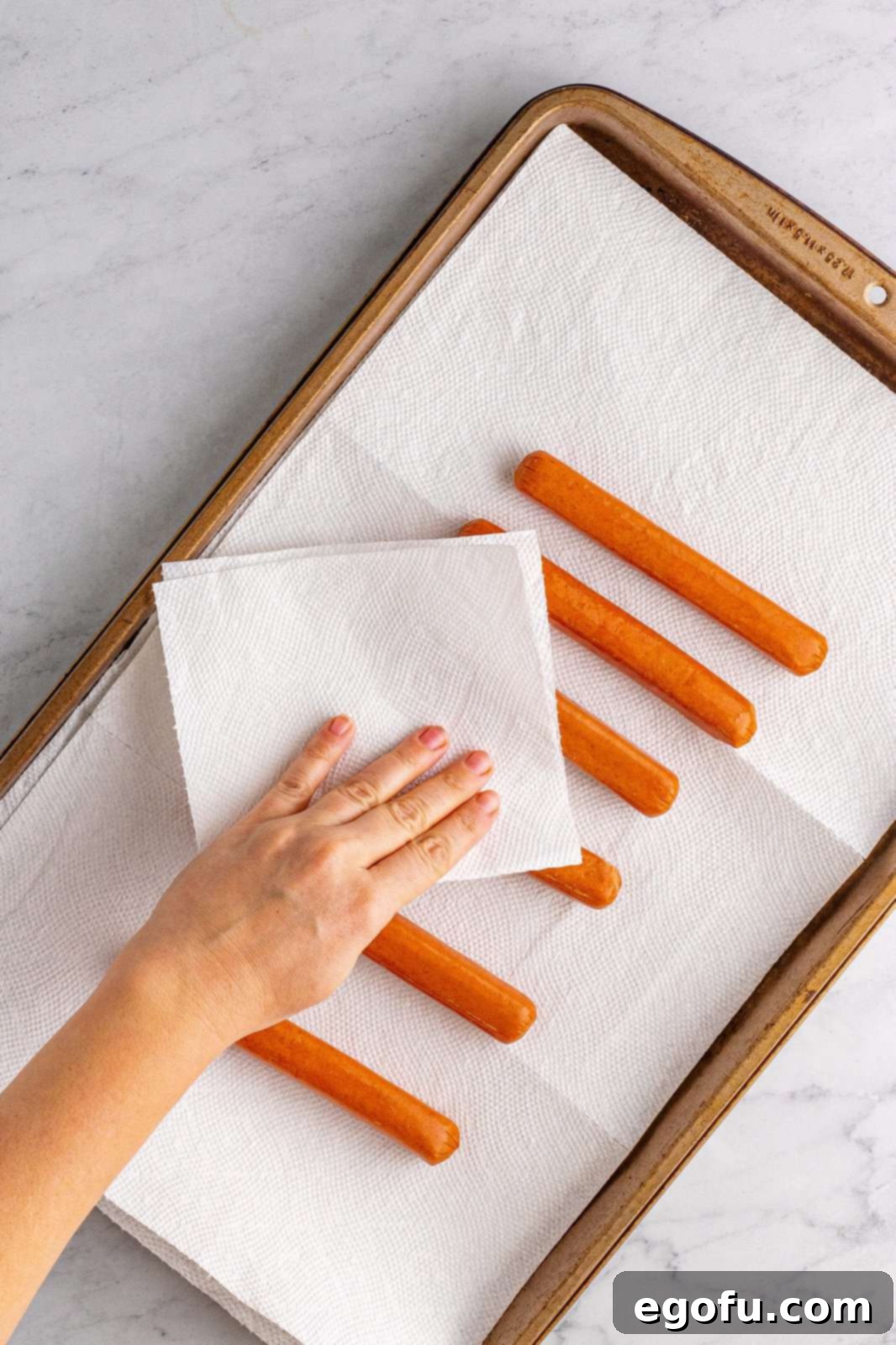A hand drying off a hot dog with a paper towel, preparing it for wrapping.