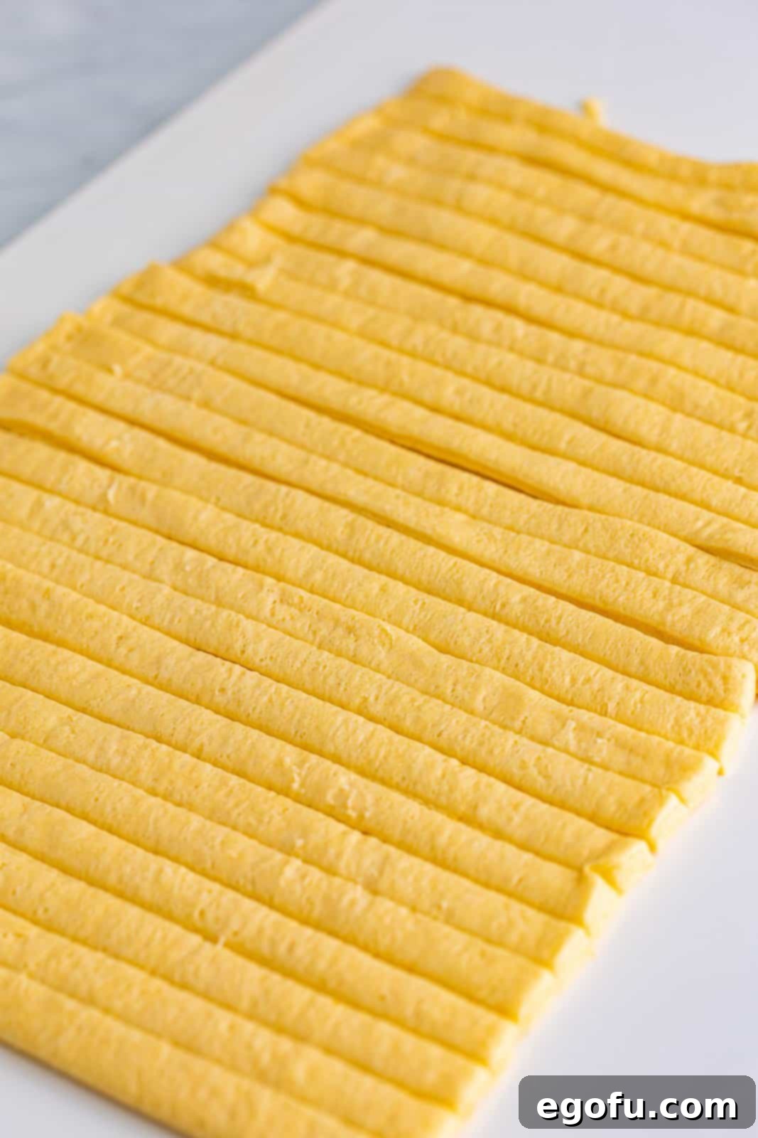 Crescent roll dough neatly cut into thin strips, ready for wrapping.