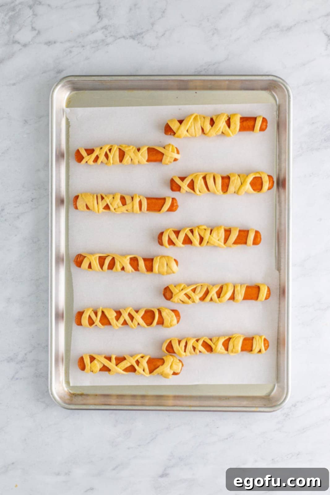Wrapped hot dogs neatly arranged on a baking sheet, ready for the oven.