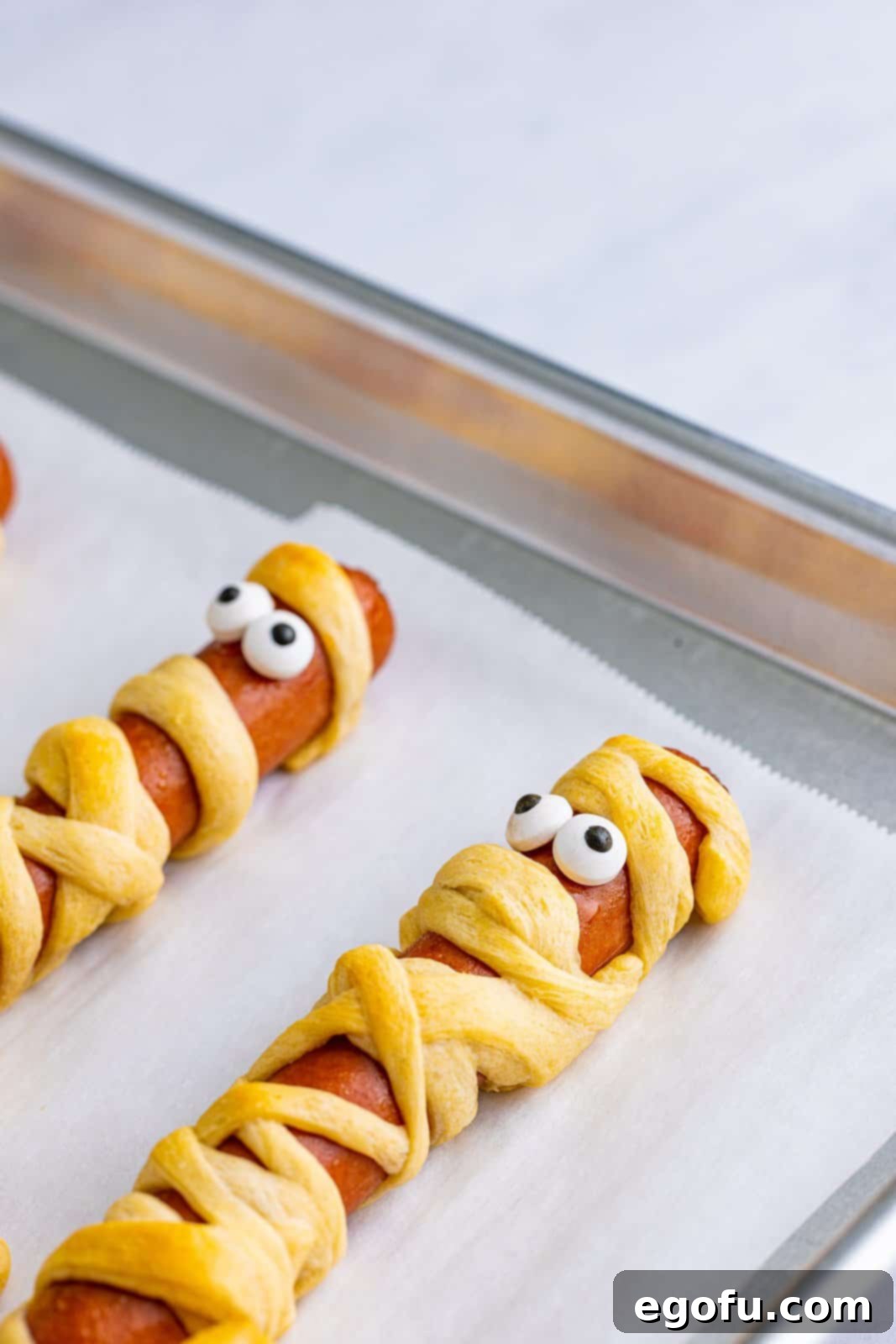 Applying candy eyes to baked Halloween Mummy Dogs using small dabs of ketchup to secure them.