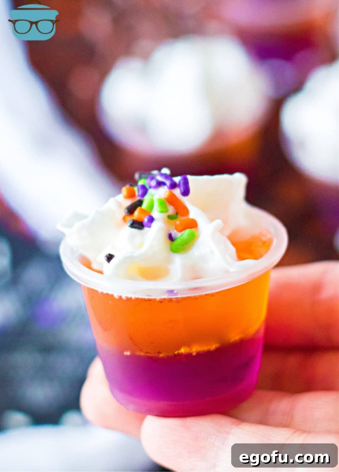 Hand holding up one of the Hocus Pocus Jell-O Shots, showcasing its vibrant purple and orange layers, ready for a festive Halloween celebration.