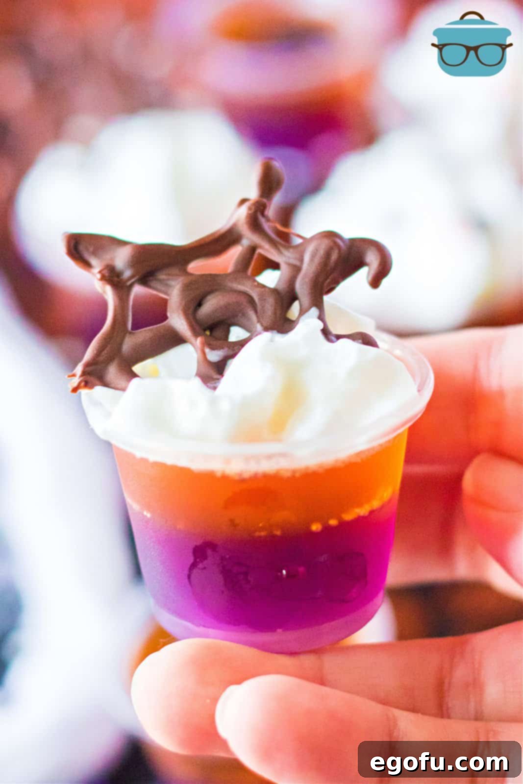 A hand elegantly holding up one of the finished Hocus Pocus Jell-O Shots, beautifully decorated with a delicate chocolate spiderweb, ready to be savored at a Halloween gathering.