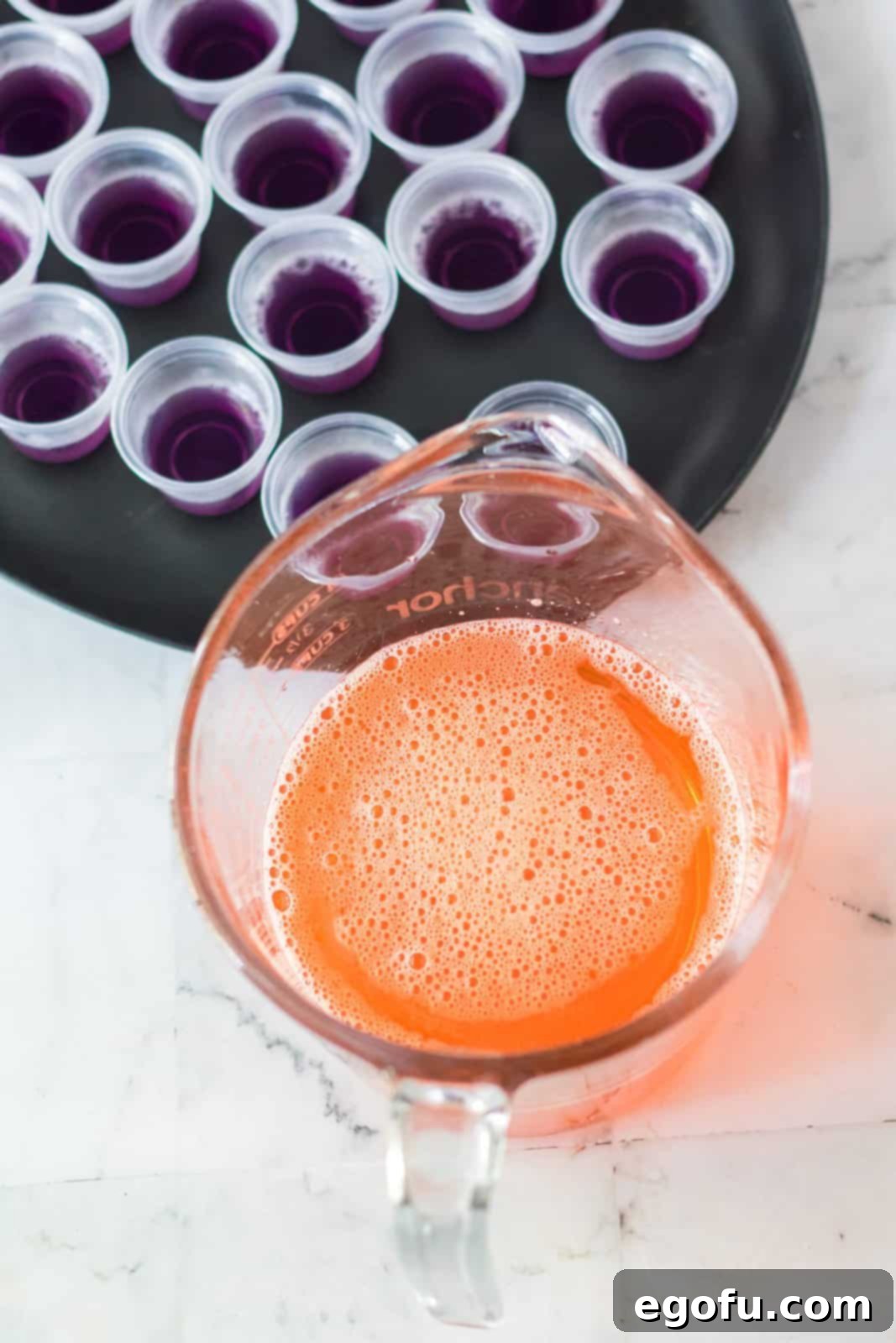 Vibrant orange Jell-O, water, and vodka expertly whisked together in a spouted measuring cup, showcasing the readiness of the second colorful layer for the Hocus Pocus Jell-O Shots.
