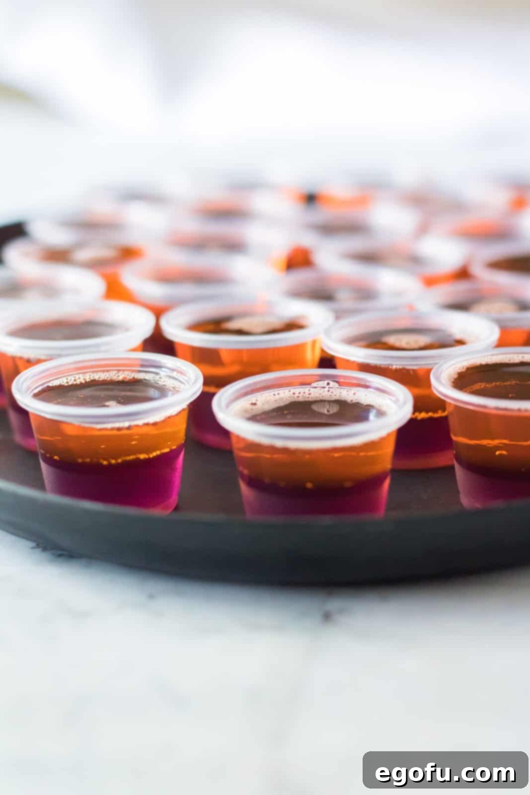 The bright orange Jell-O mixture meticulously poured on top of the already set purple Jell-O mixture in small plastic cups, creating distinct, vibrant layers for the Hocus Pocus Jell-O Shots.