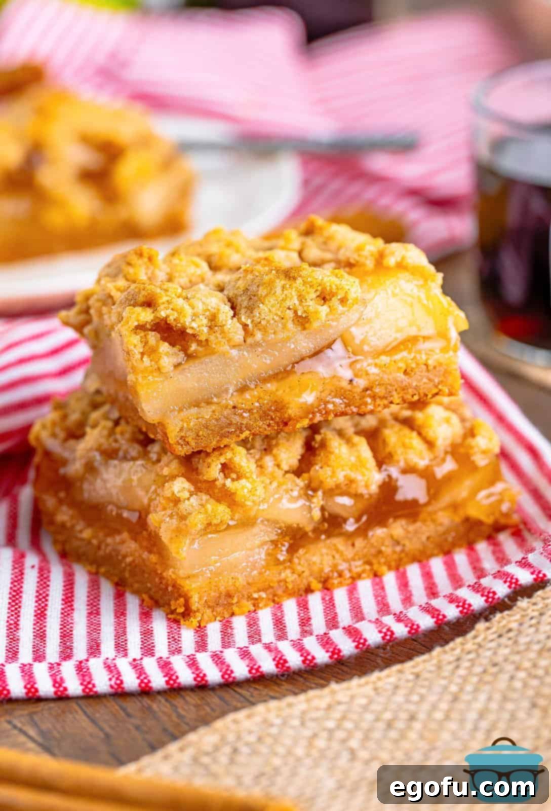 Classic Apple Crumble Bars 2 Two stacked Apple Crumble Bars showcasing their golden crust, apple filling, and crumbly topping on a festive red and white linen, promising a delicious bite.
