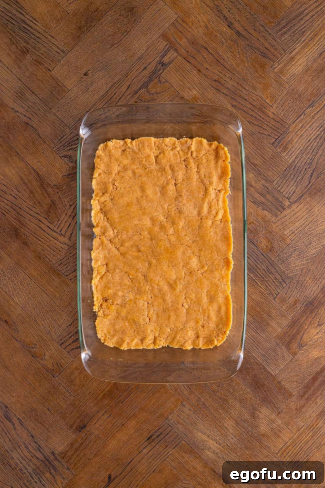 Classic Apple Crumble Bars 10 A uniform layer of the crust/crumble mixture is firmly pressed into the bottom of a rectangular baking pan, forming the base for the apple bars.