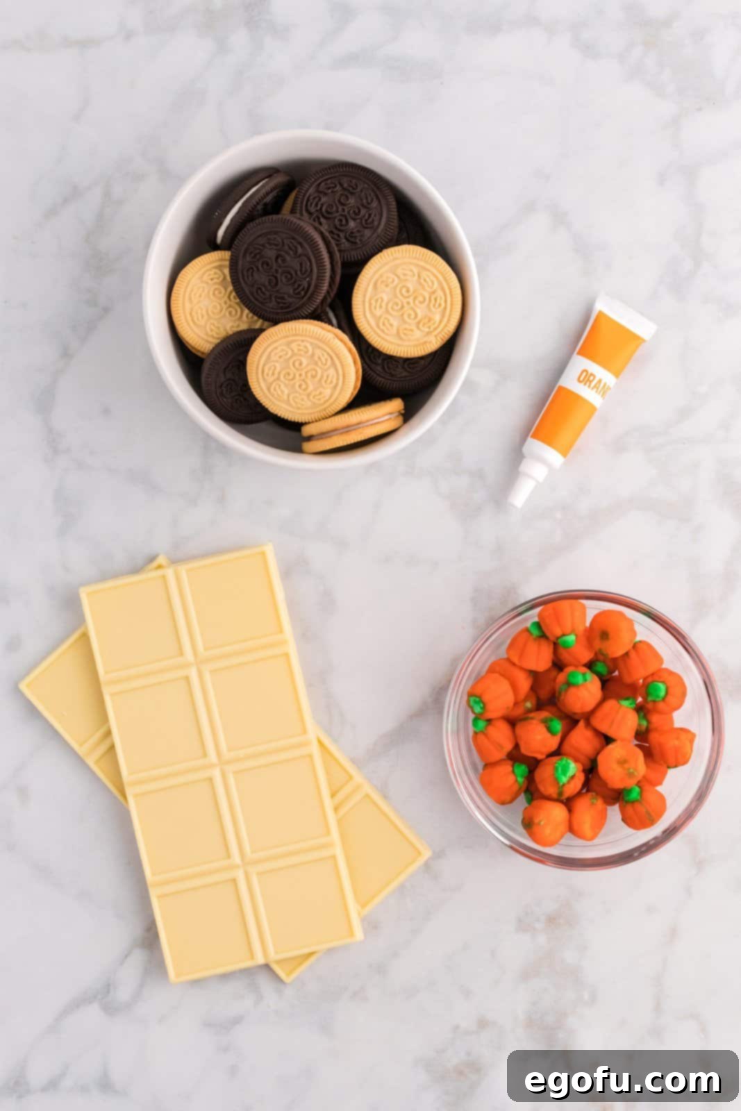 Spiced Pumpkin Patch Cookies 4 Ingredients for Pumpkin Patch Cookies laid out: vanilla and chocolate sandwich creme cookies, white melting chocolate, orange gel food coloring, and mellowcreme pumpkin candies.