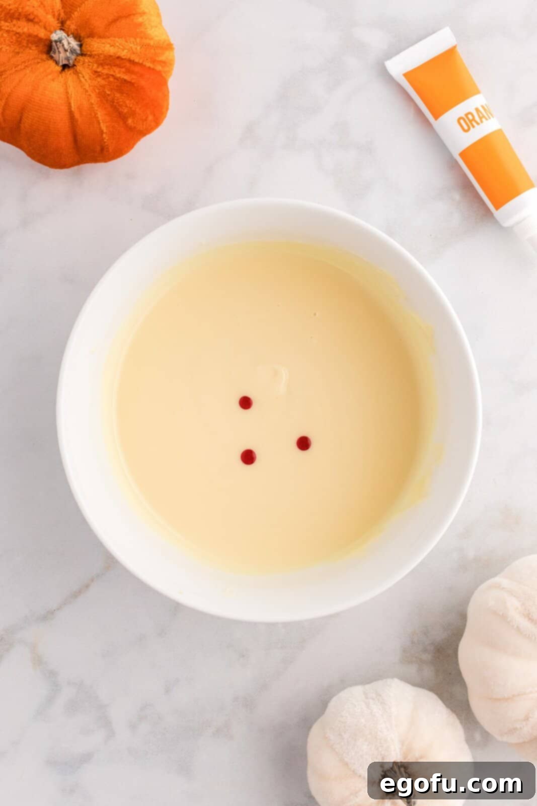 Spiced Pumpkin Patch Cookies 7 Melted white chocolate in a bowl with orange gel food coloring being stirred in, creating a vibrant orange hue.