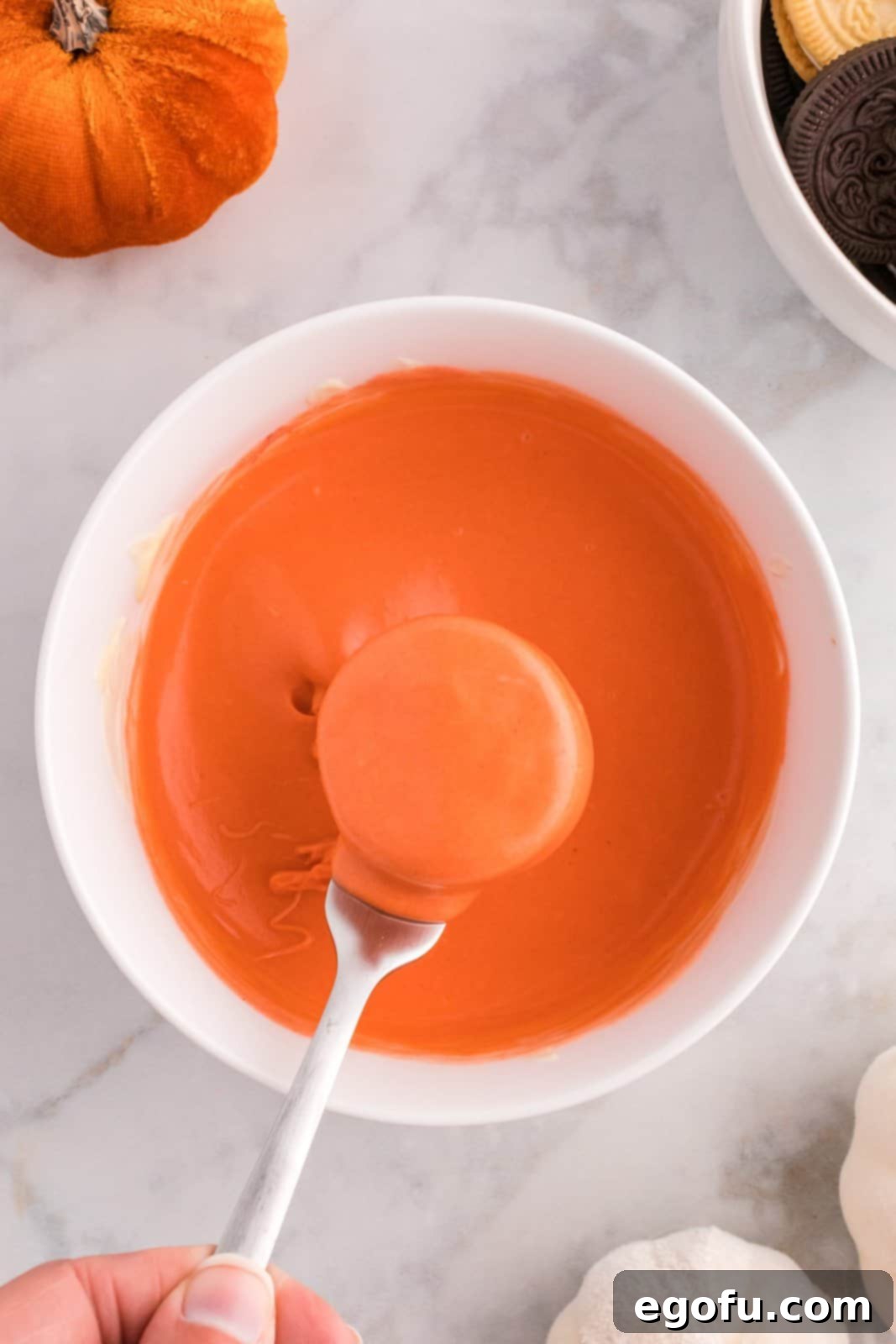 Spiced Pumpkin Patch Cookies 8 An Oreo cookie being lifted out of the orange melted chocolate with a fork, coated evenly.