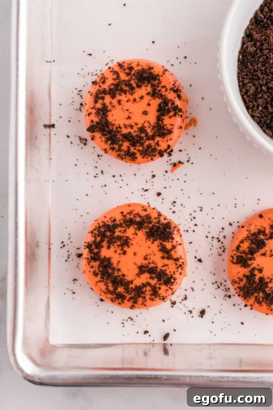 Spiced Pumpkin Patch Cookies 9 Freshly dipped orange cookies on a baking sheet, being sprinkled with chocolate cookie crumbs.