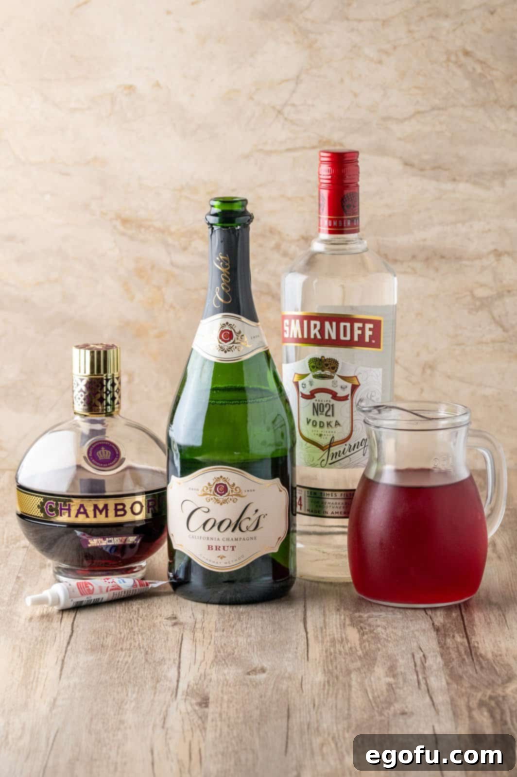 Crimson Embrace Elixir 3 All ingredients laid out for Vampire's Kiss Cocktail: red decorating gel, vodka, raspberry liqueur, cranberry juice, and champagne.