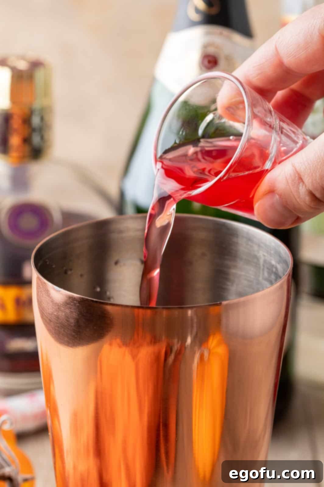 Crimson Embrace Elixir 7 Cranberry juice being poured into the cocktail shaker with other ingredients.