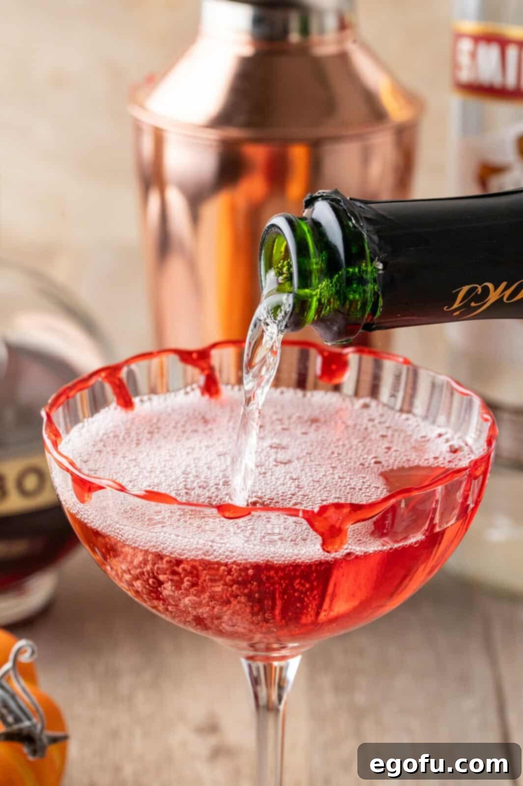 Crimson Embrace Elixir 9 Champagne being carefully poured into the cocktail glass, topping the red mixture.
