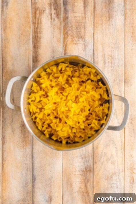 Campus Noodle Comfort 11 Egg noodles in a pot with seasoned chicken stock, stirring.