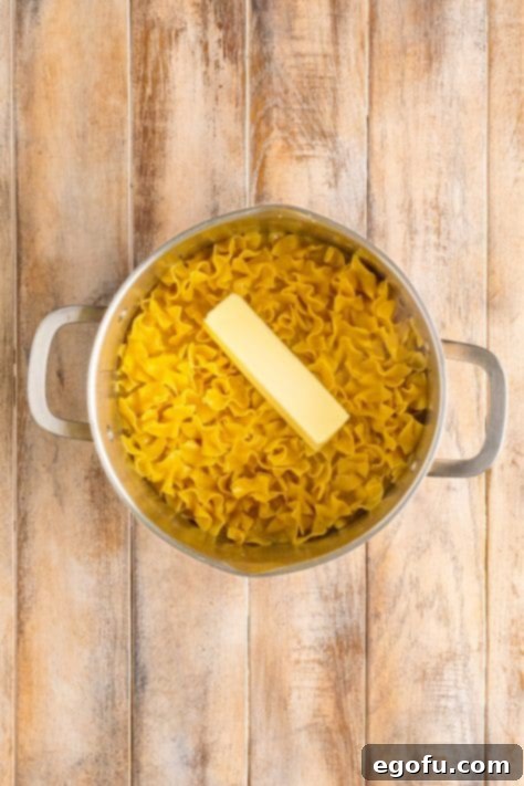 Campus Noodle Comfort 13 A stick of butter resting on top of hot egg noodles in a pot.