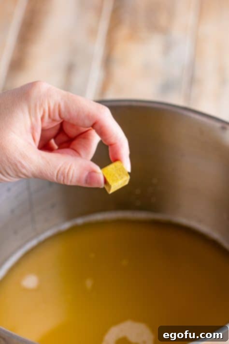 Campus Noodle Comfort 10 A bouillon cube being held over a pot of chicken stock.