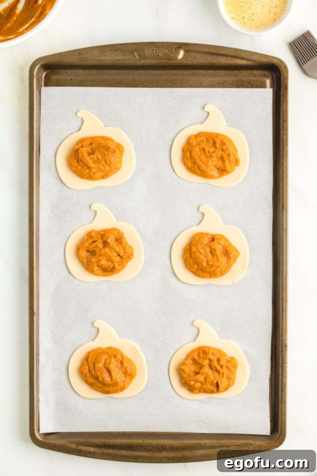 Cut pumpkin pie crust shapes on parchment lined paper with filling placed in center.
