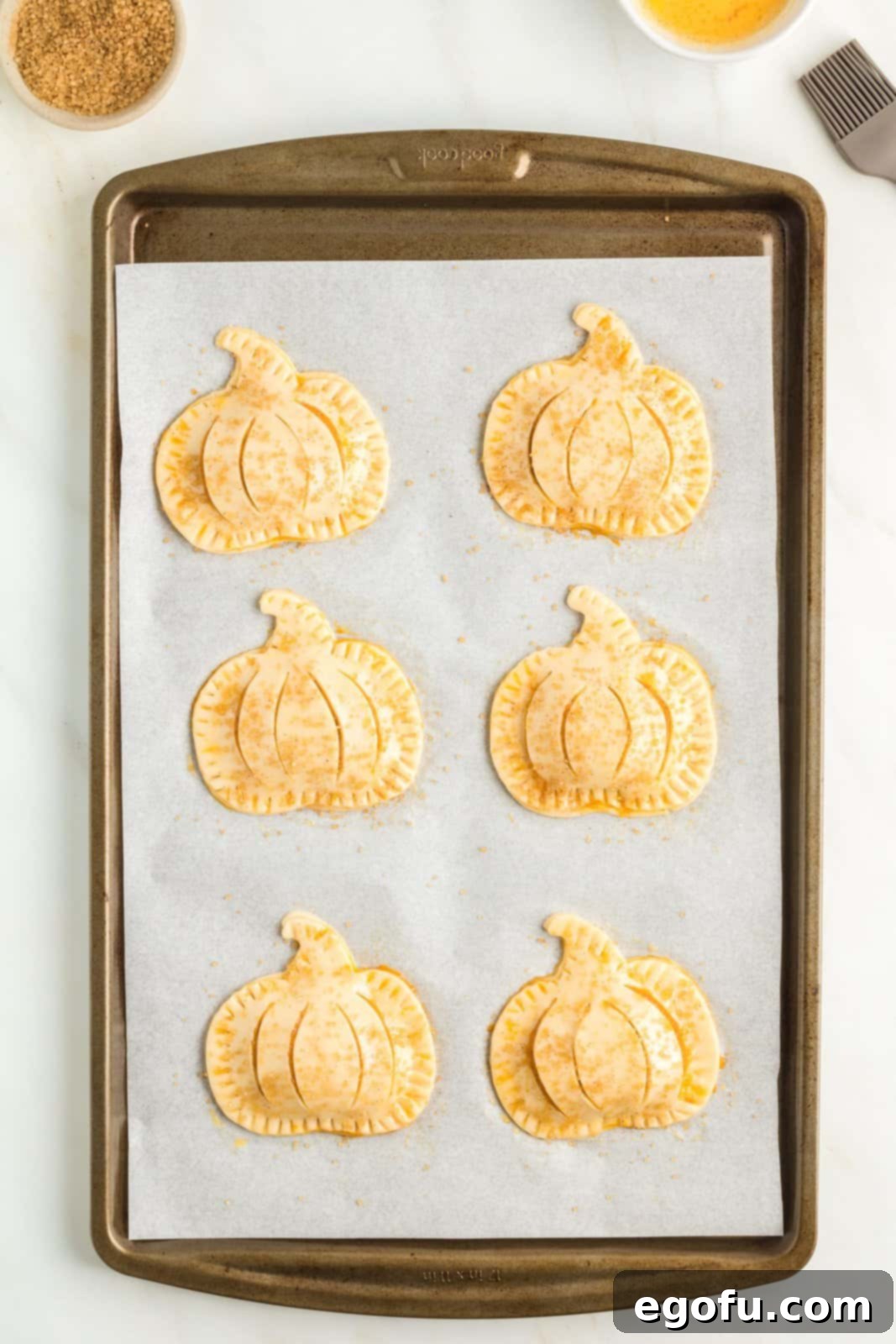 Hand pies on parchment lined baking sheet brushed with egg wash and sugar mixture.