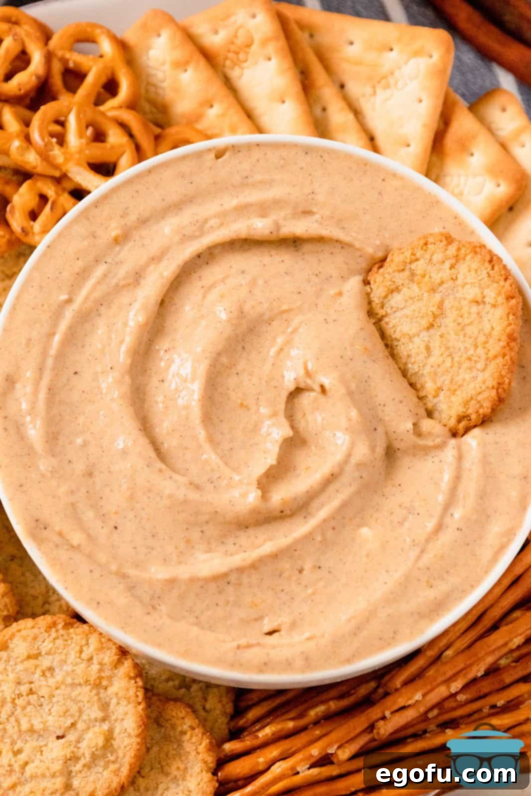 Overhead of Pumpkin Dip in white bowl with cookie in bowl and different dippers around bowl.