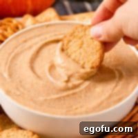 Square image close up of hand dipping a cookie into Pumpkin Dip in bowl.