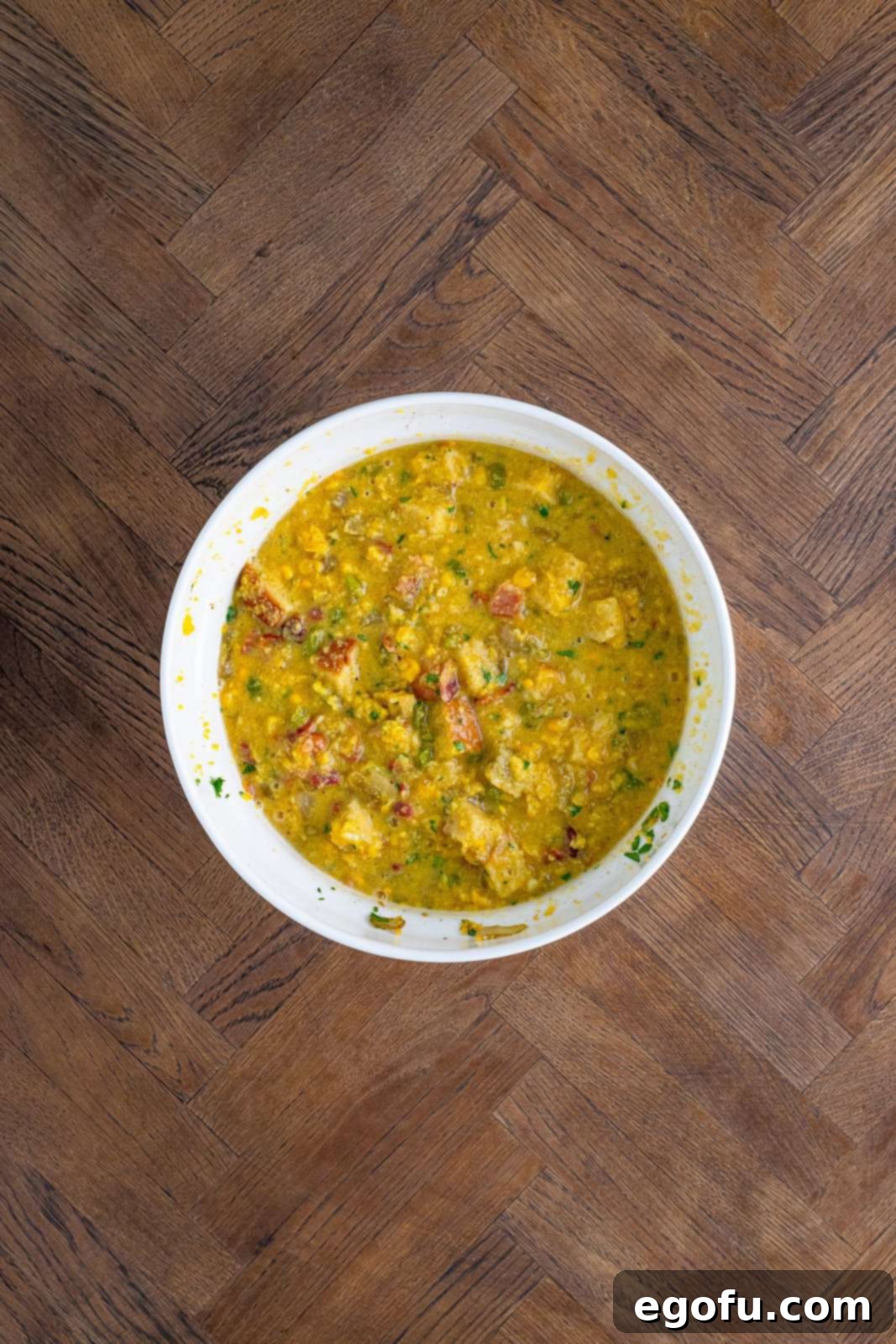 Corn, egg and stock mixture added to bowl with breads, bacon and vegetables mixed together.