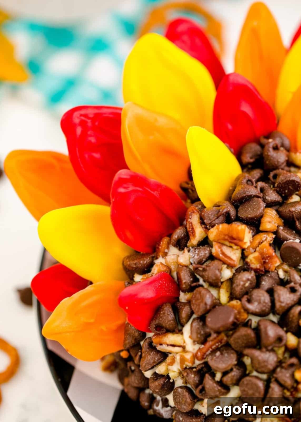 Colorful candy melt feathers being carefully pressed into the back of the cheeseball, creating a turkey's tail.